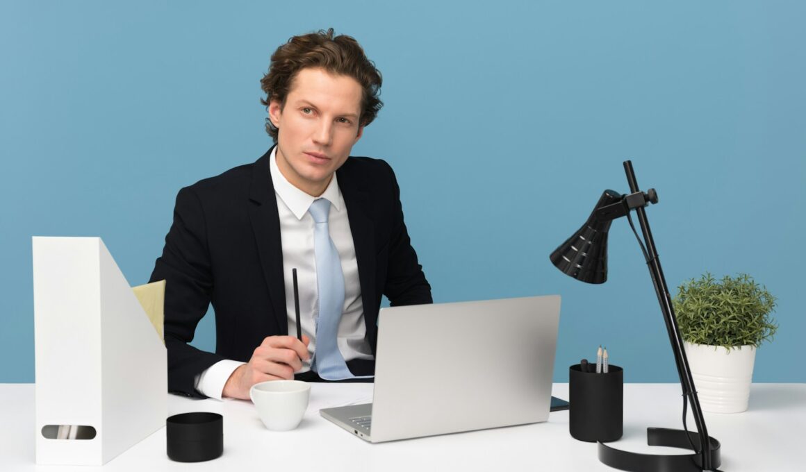 man sitting on chair beside laptop computer and teacup